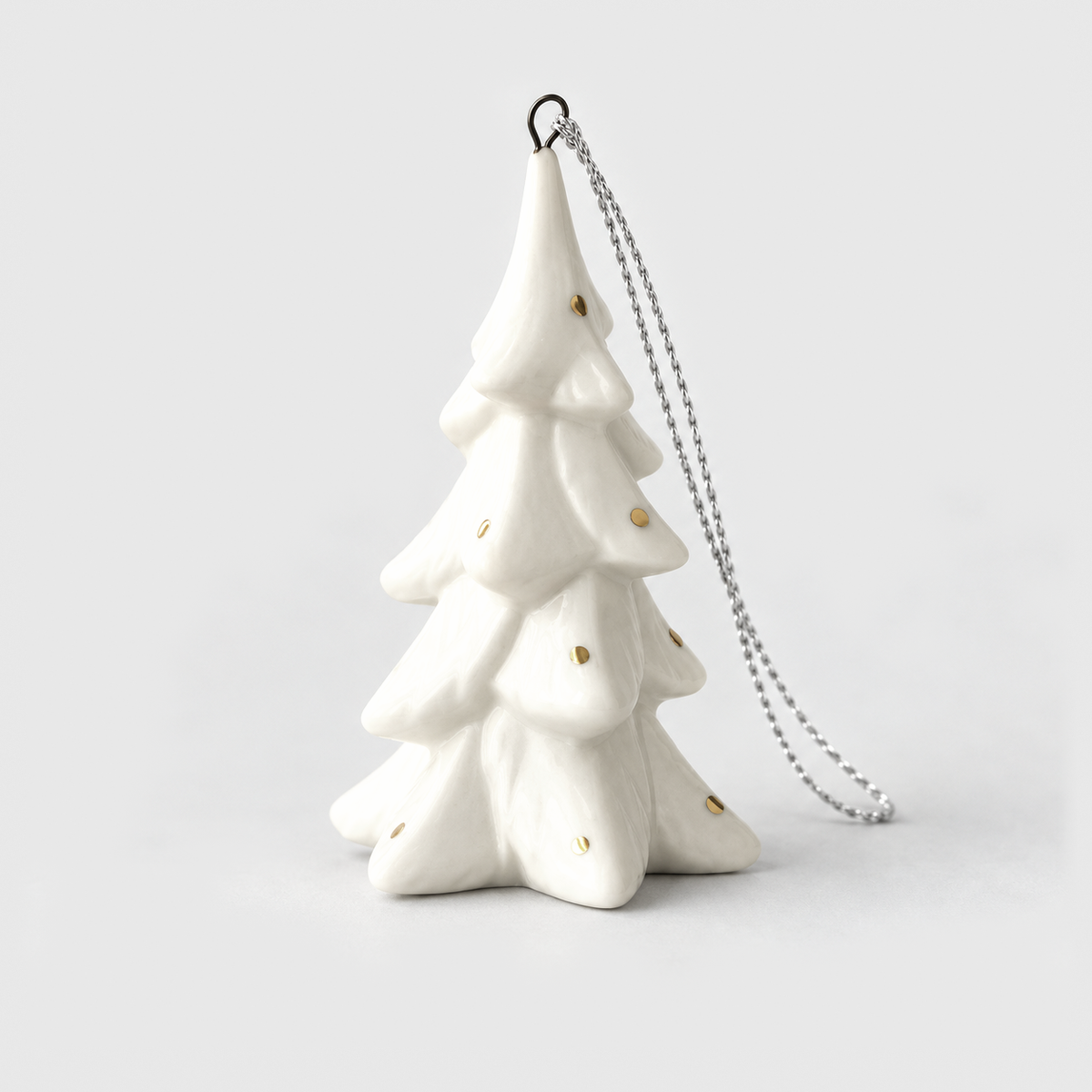Tall slim white ceramic Christmas tree ornament in the Spruce style with drooping snowy branches and small gold flecks, on a light gray background