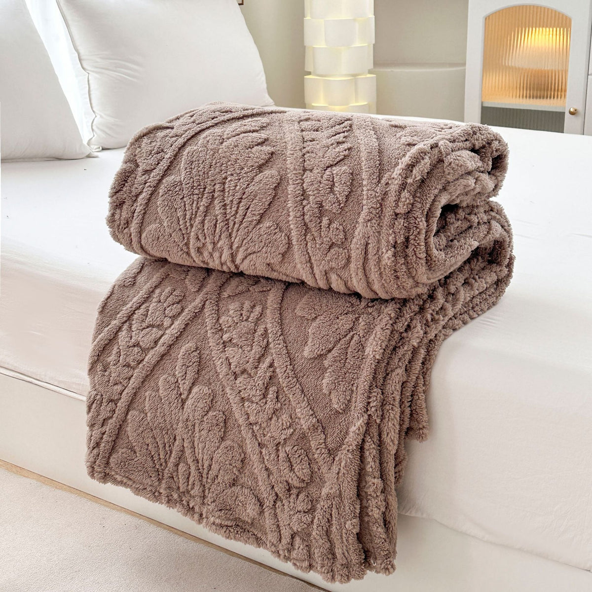 Brown embossed fleece blanket folded and rolled on a bed
