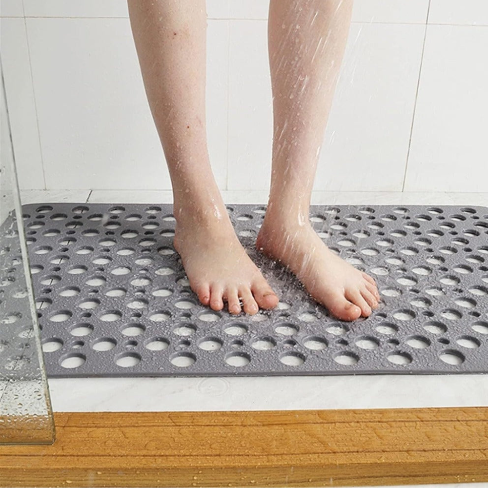Bare feet standing on the gray shower mat while water runs over it and drains through the holes