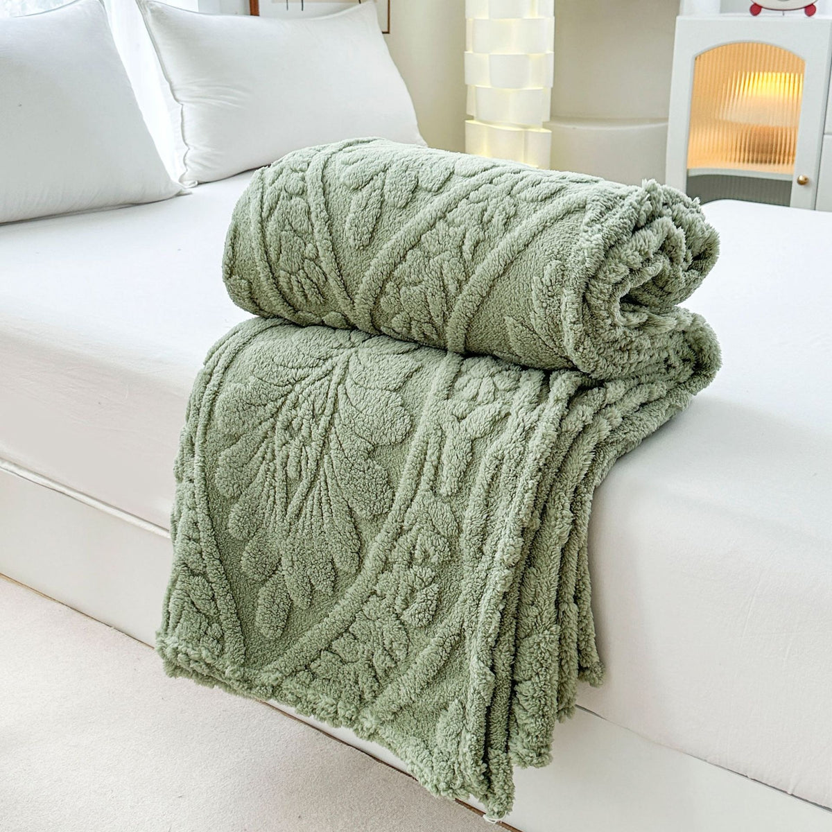 Green embossed fleece blanket folded and rolled on a bed