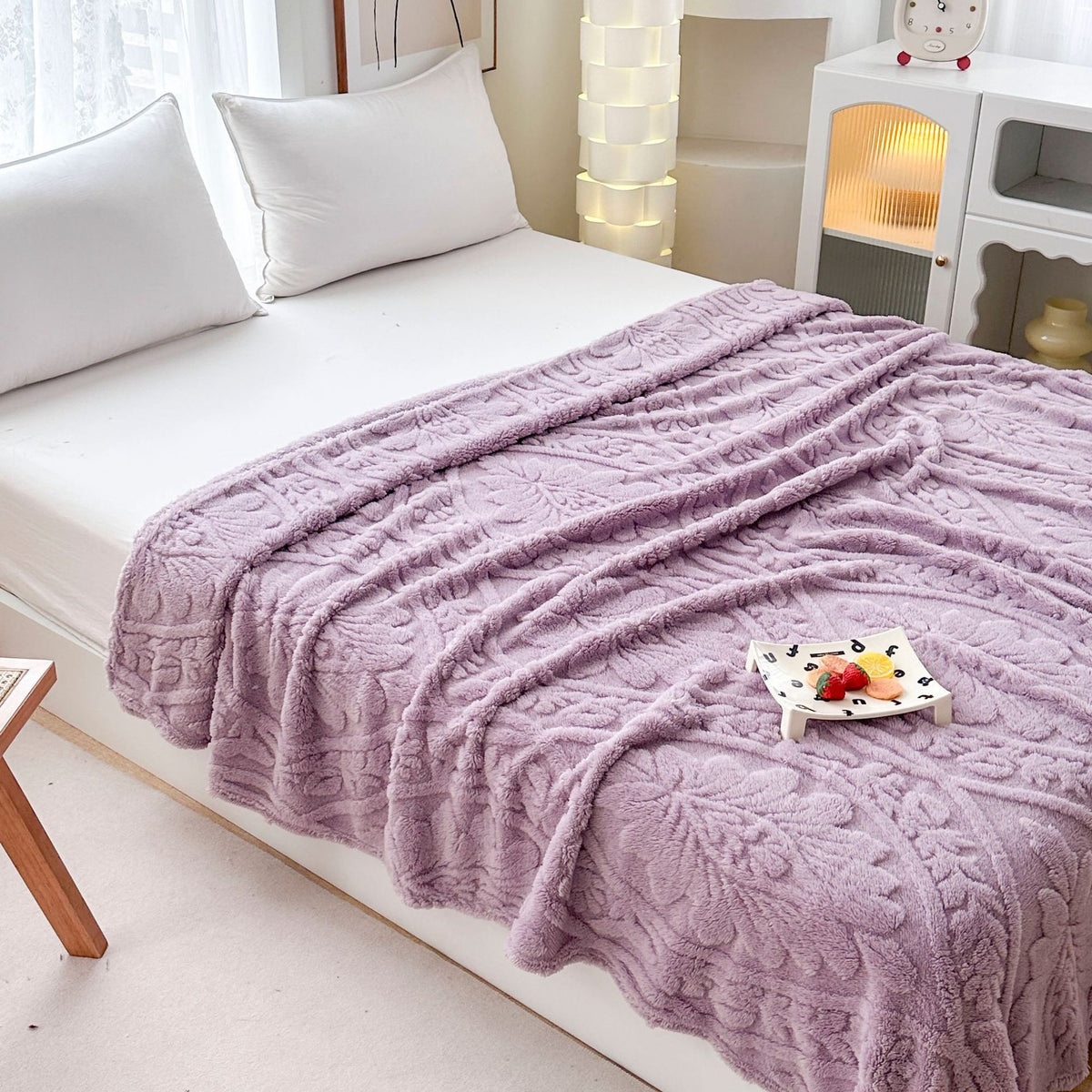 Purple damask fleece blanket spread across a bed with a small tray