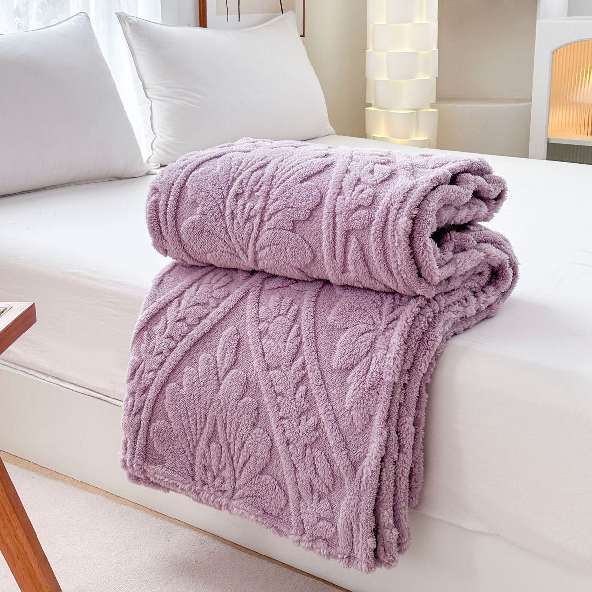 Purple embossed fleece blanket folded and rolled on a bed