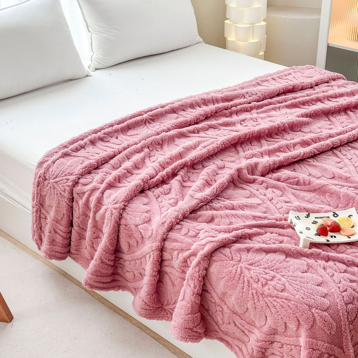 Pink damask fleece blanket spread across a bed with a small tray