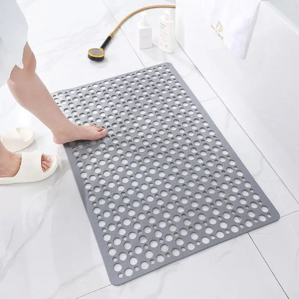 Gray non slip shower mat on a white tiled bathroom floor with a foot stepping onto it