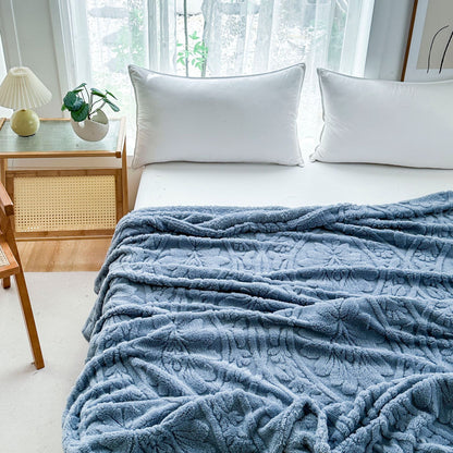 Blue embossed fleece blanket spread across a bed, showing the raised damask pattern