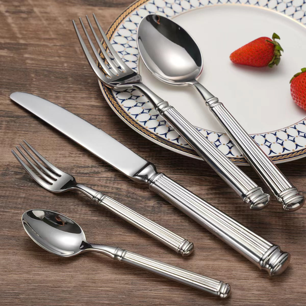 Fluted stainless steel cutlery beside a blue patterned plate with strawberries on a dark wood table