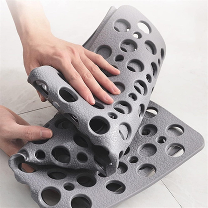 Hands folding the gray shower mat, showing that it is flexible and revealing the suction cup underside