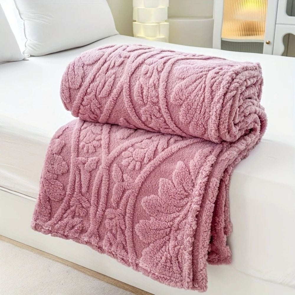 Pink embossed fleece blanket folded and rolled on a bed