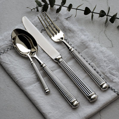 Dinner spoon, dinner knife, dinner fork and teaspoon on grey linen with a eucalyptus stem above, showing the fluted handles