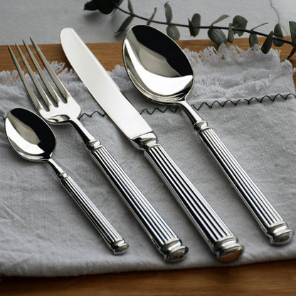 Five pieces of mirror polished fluted cutlery laid on grey linen over a wooden board, with a eucalyptus sprig behind