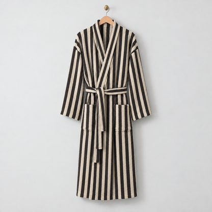 Long black and cream striped fleece bathrobe with a tie belt, hanging on a wooden hanger on a light gray wall