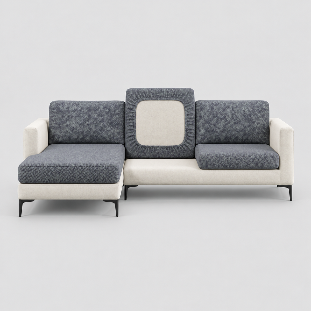 Cream L-shaped sofa face-on with charcoal stretch covers on its seat, back and chaise cushions, one back cushion turned to show the elastic underside