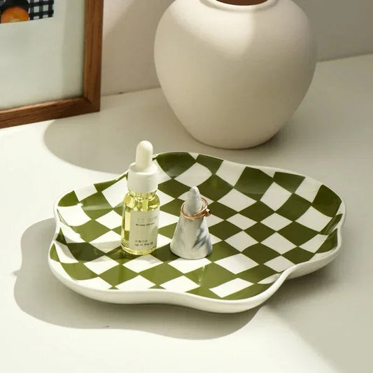 Green and white checkered ceramic tray on a pale sideboard holding a small bottle and a ring, its shallow white rim following the wavy edge