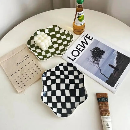 Green and black checkered ceramic trays on a round white table, the green one holding a small white candle