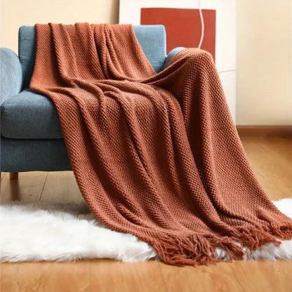 Rust pebble knit throw blanket draped over a blue sofa with tassels on a white rug