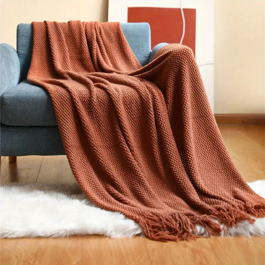 Rust pebble knit throw blanket draped over a blue sofa with tassels on a white rug