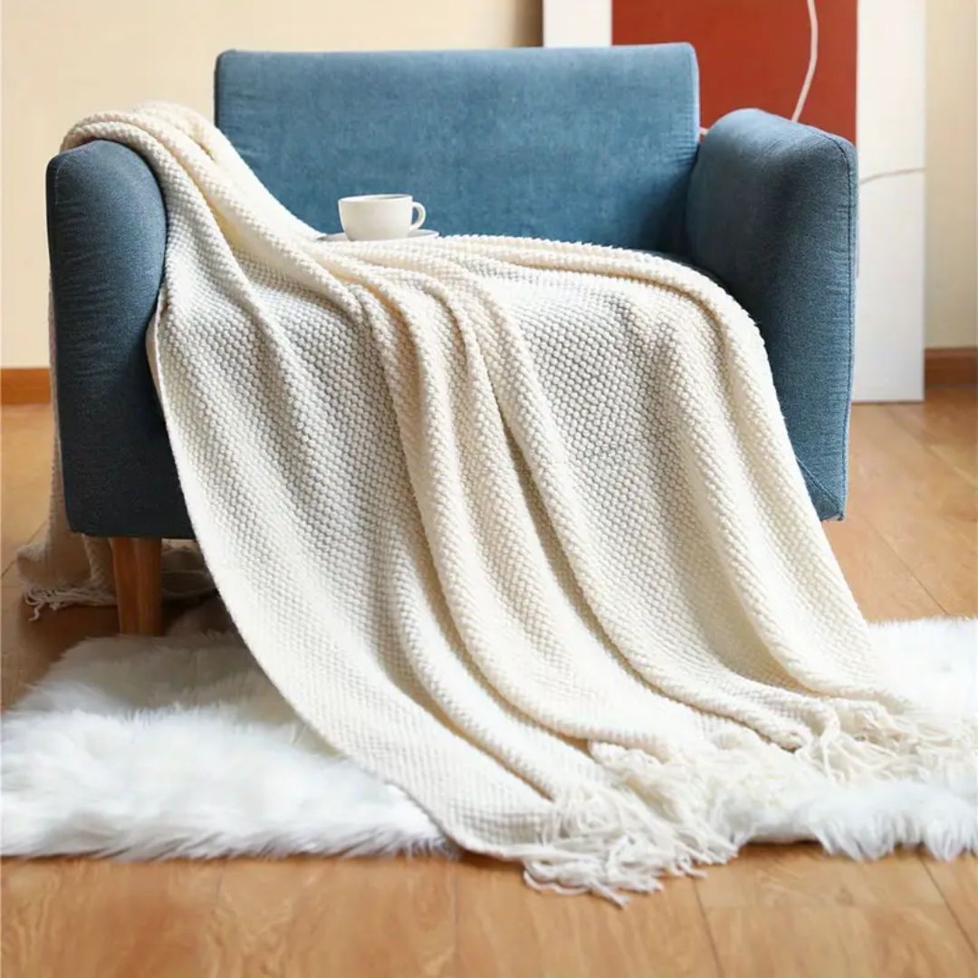 Cream pebble knit throw blanket draped over a blue armchair onto a white rug