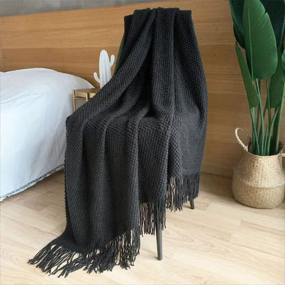 Black pebble knit throw blanket hung over a chair with long tassels