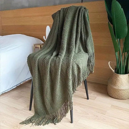 Olive pebble knit throw blanket draped over a chair beside a bed