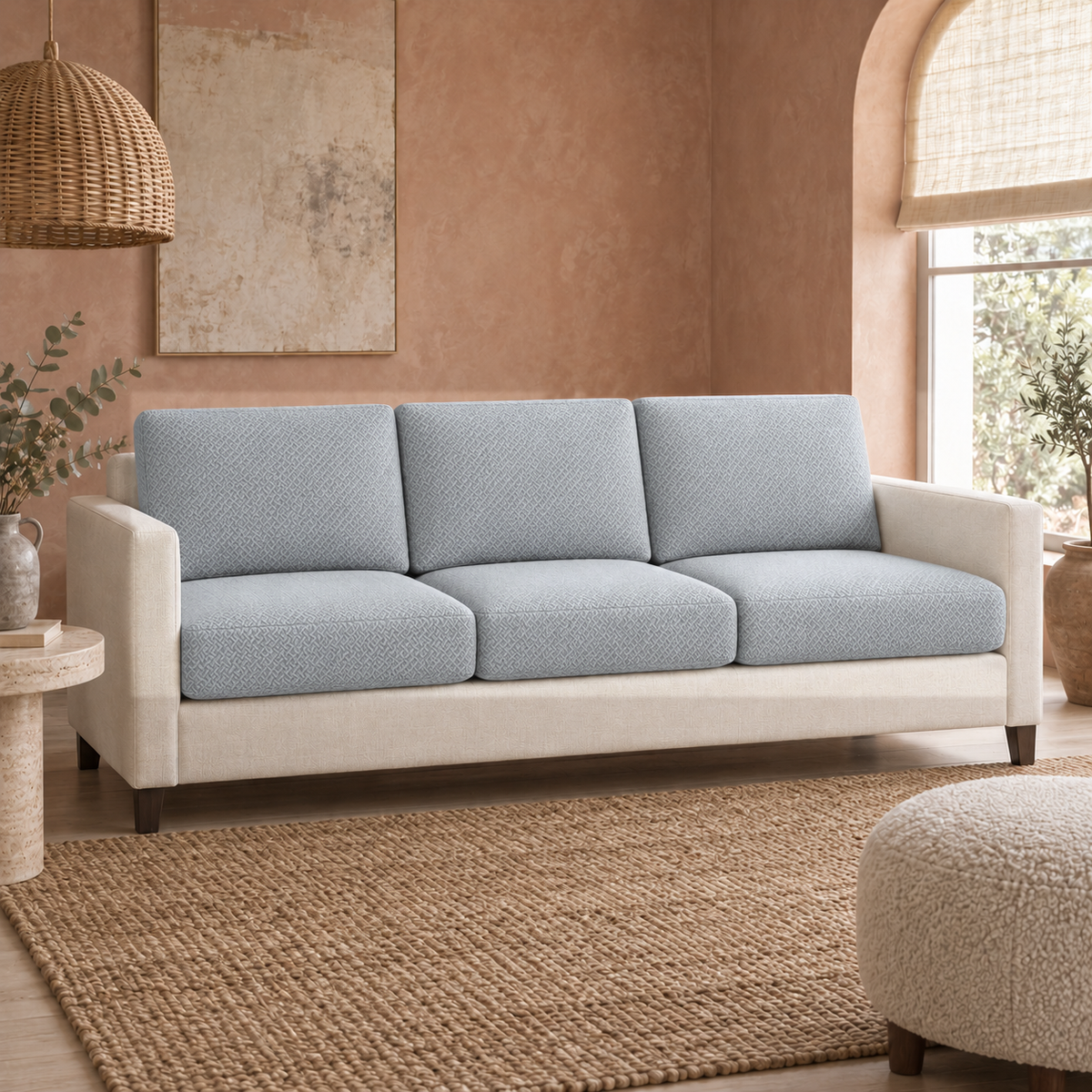 Three-seat sofa with grey cushion covers against a soft clay-colored wall with a jute rug and an arched window