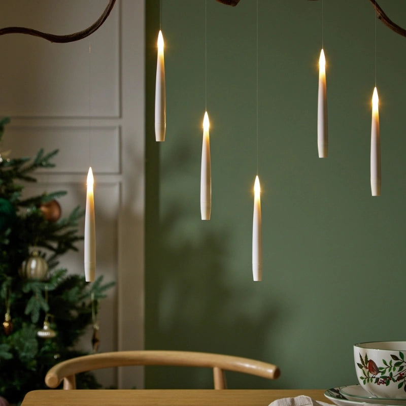 Six ivory LED taper candles hanging on fine lines against a green wall