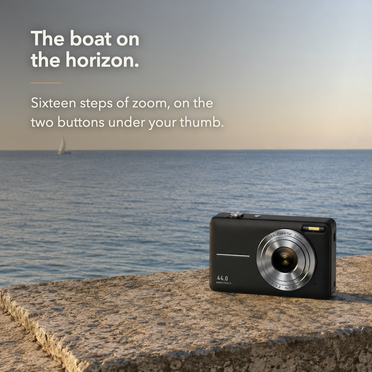 Text card. Black compact digital camera standing on a stone harbour wall above the sea with a distant sailing boat near the horizon, headed The boat on the horizon, above the line Sixteen steps of zoom, on the two buttons under your thumb