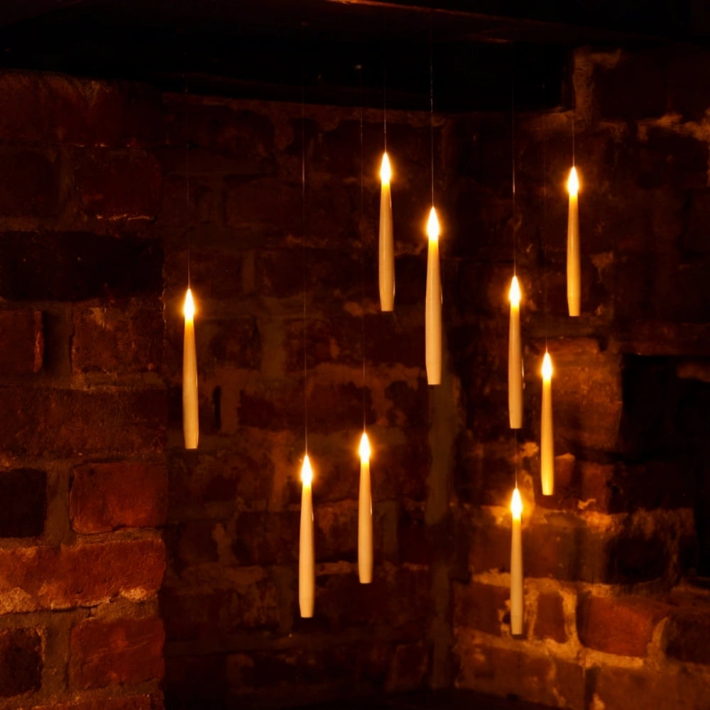 Ten floating LED candles hanging at staggered heights against a brick wall