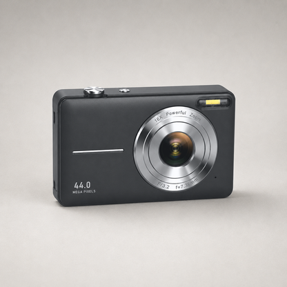 Black compact digital camera on a plain grey studio background, front three-quarter view showing the silver lens ring, the shutter button on the top plate and the flash window at the top right