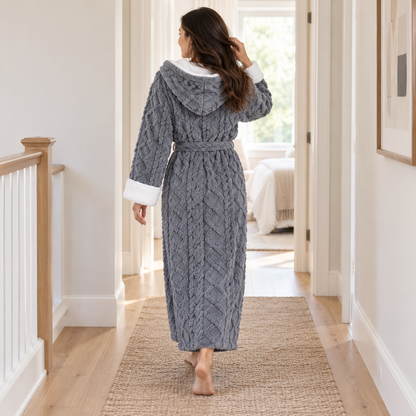 Woman in a gray plush bathrobe walking away down a hallway, showing the hood and the cable pattern on the back