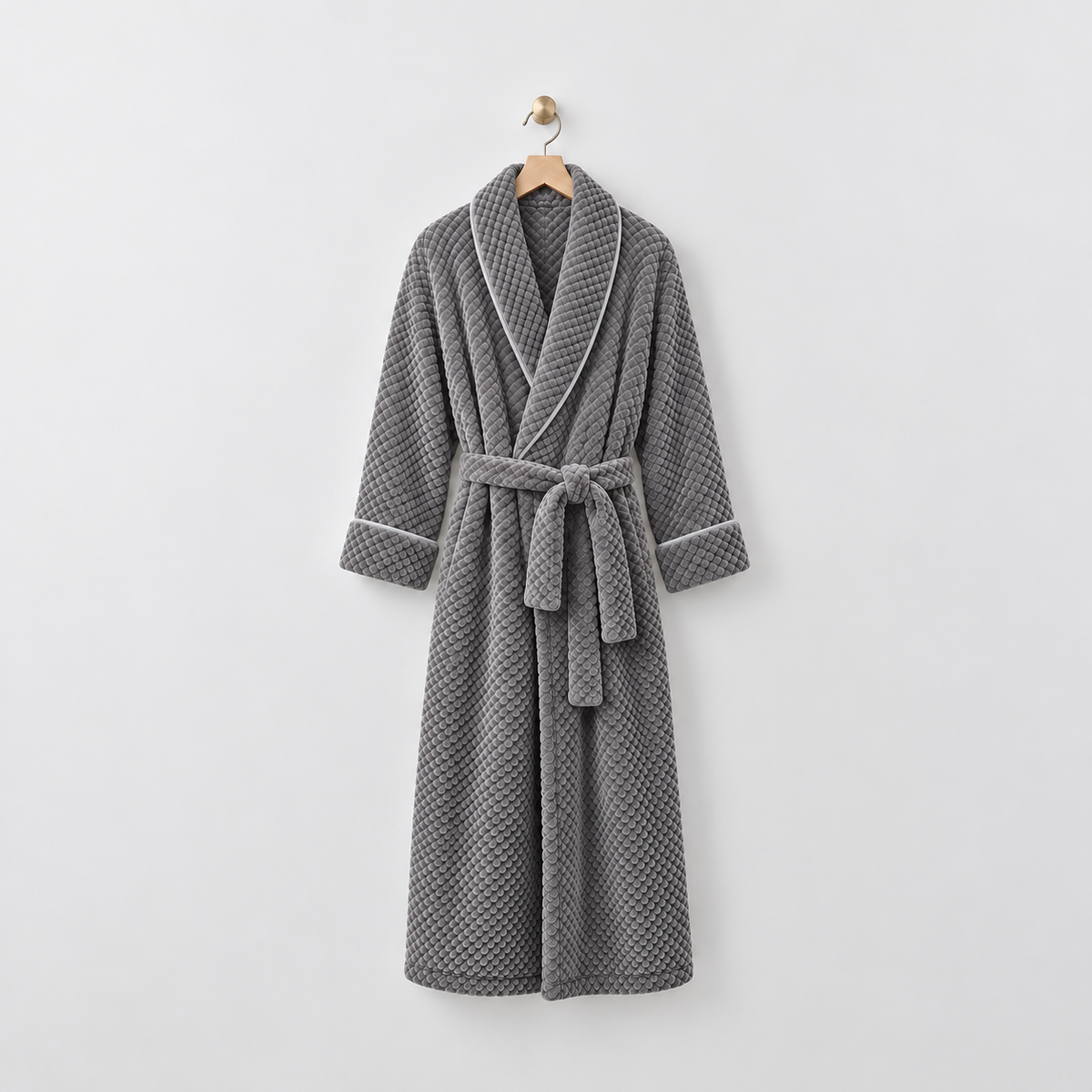 Long gray waffle-textured fleece bathrobe with a shawl collar and tied belt, hanging on a wooden hanger from a brass hook on a light gray wall