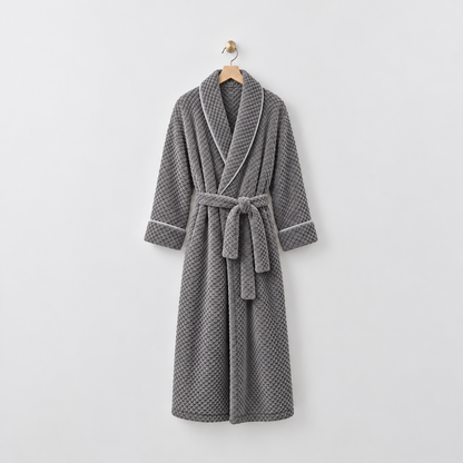 Long gray waffle-textured fleece bathrobe with a shawl collar and tied belt, hanging on a wooden hanger from a brass hook on a light gray wall