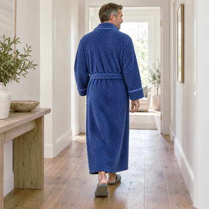 Back view of a man walking down a bright hallway in an ankle-length royal blue waffle fleece bathrobe with the belt tied