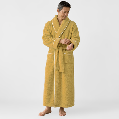 Man rolling back the cuff of an ankle-length mustard fleece bathrobe, barefoot on a light grey backdrop