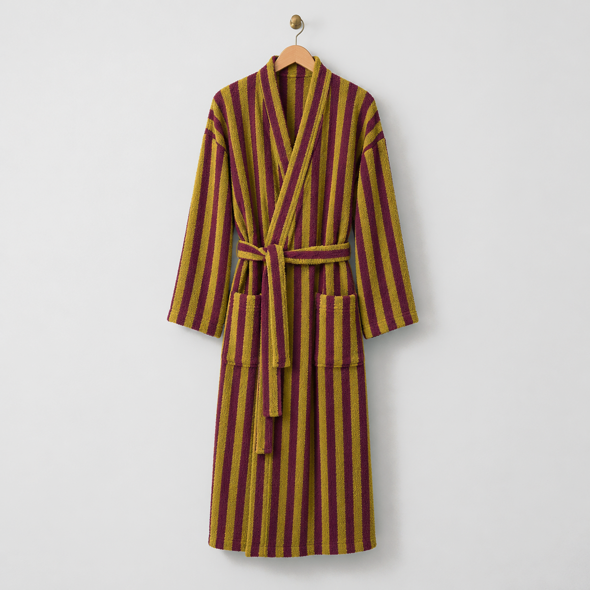 Long mustard and burgundy striped fleece bathrobe with a tie belt, hanging on a wooden hanger on a light gray wall