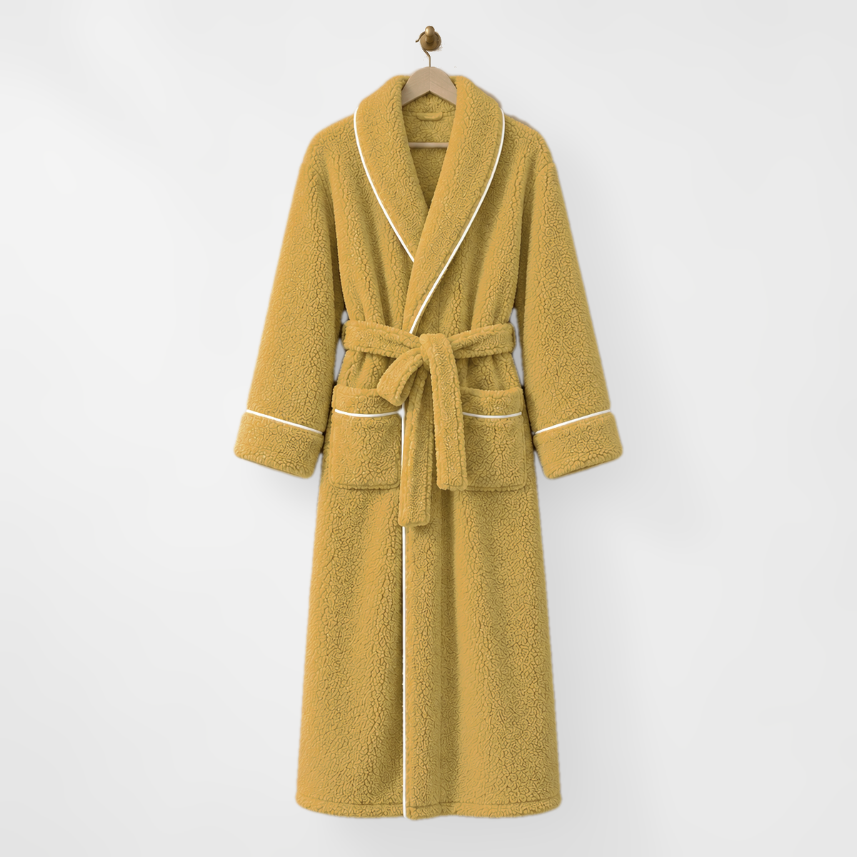 Long mustard fleece bathrobe with white piping, hanging on a wooden hanger from a brass hook on a light grey wall