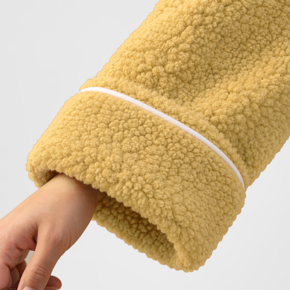 Close-up of the mustard bathrobe's turned-back cuff with white piping and the curly fleece pile