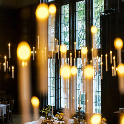 Floating LED candles beside tall daylit windows in a candlelit hall