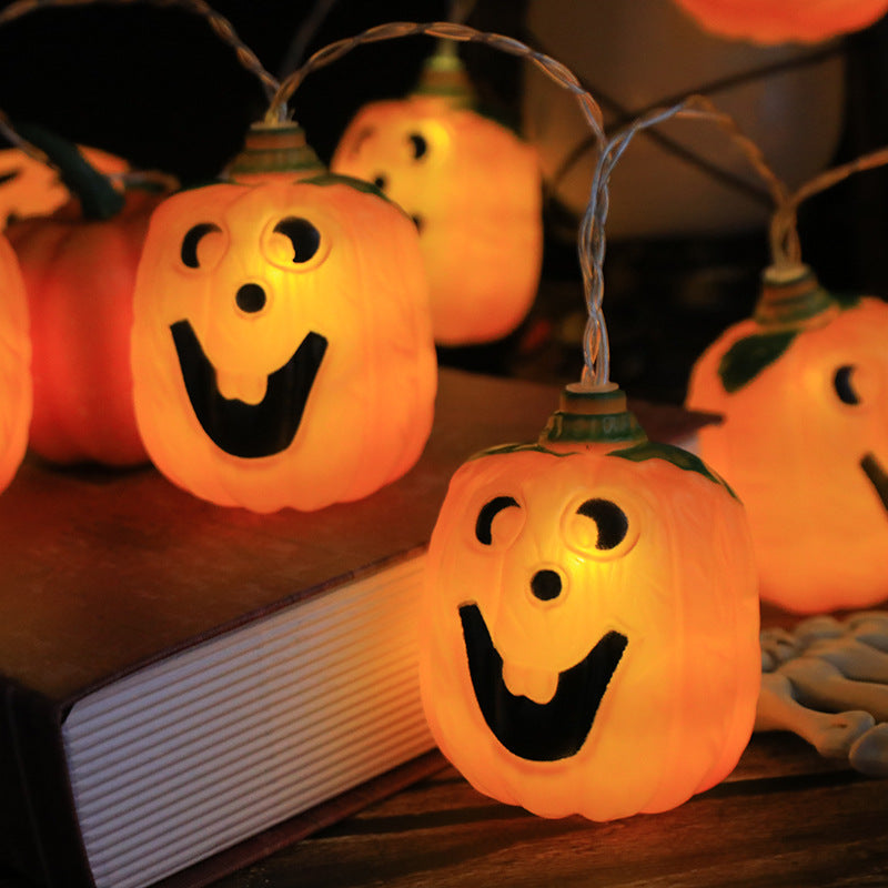 Close view of a lit jack-o'-lantern string light beside a book, the painted black grin clear against the amber glow