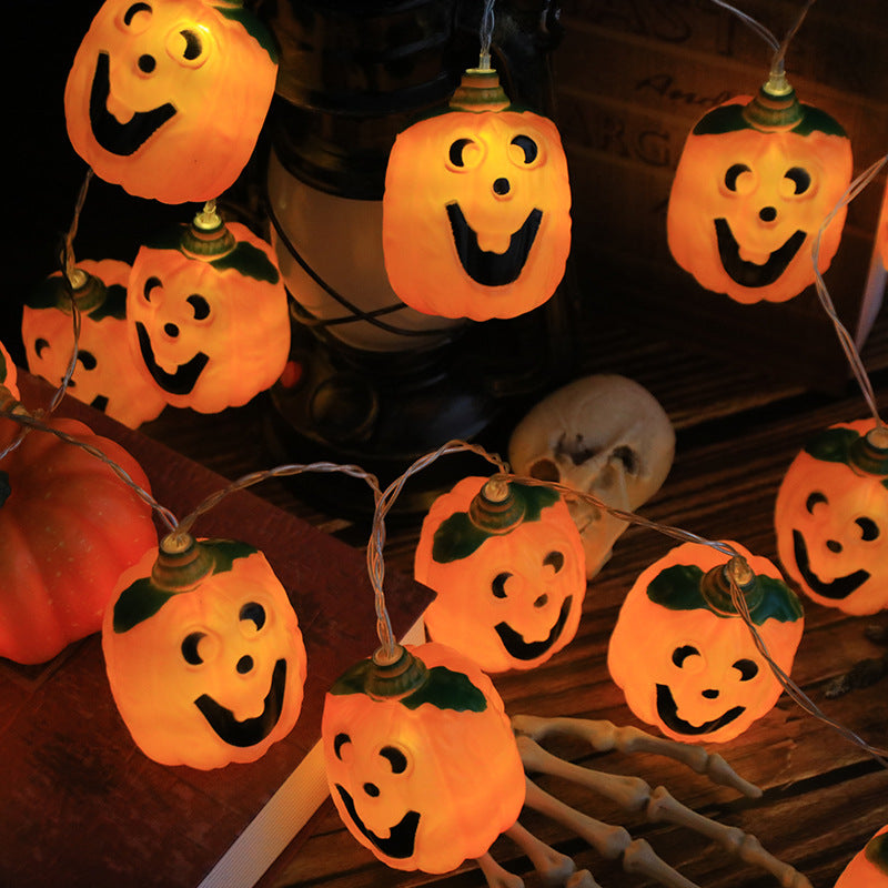 Jack-o'-lantern string lights draped around a lantern and a small skull on a wooden table