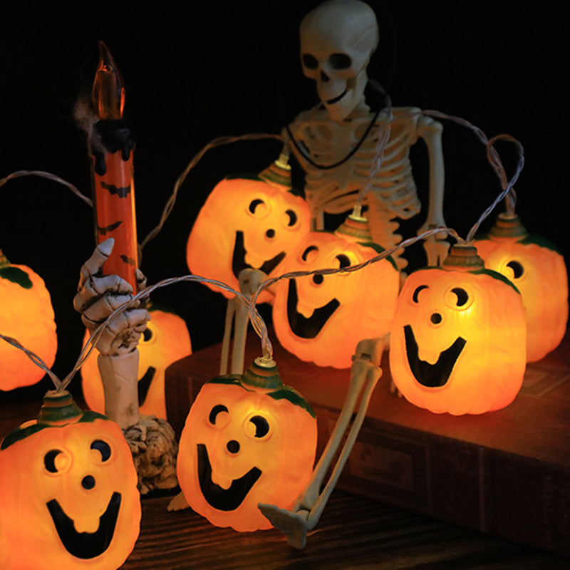 Glowing jack-o'-lantern string lights around a seated skeleton and a red candle