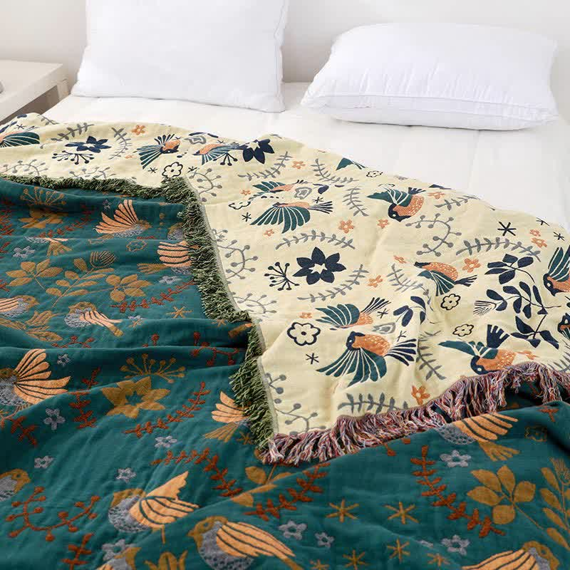 The teal bird throw on a bed with its cream side turned back over the pillow end, showing navy and orange birds and both fringes