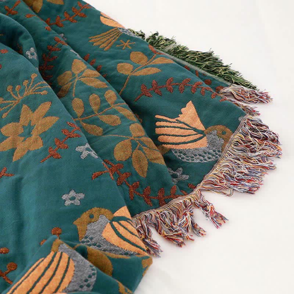 A corner of the teal side with a golden bird, rust red sprigs and leaves, and the green and multicolored fringes meeting at the corner
