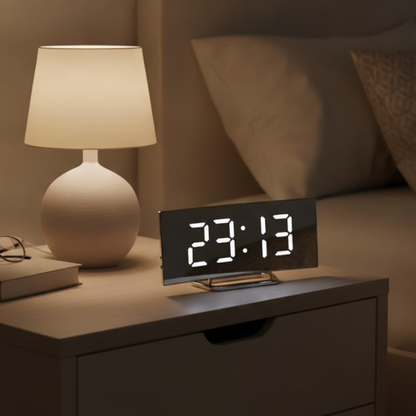 Curved LED alarm clock with white display beside a bedside lamp
