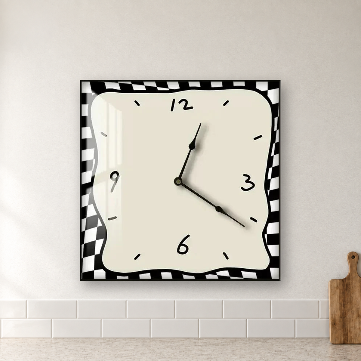 Square wall clock with a wavy doodle-style outline, a beige face and a black and white checkered border, hanging centred on a kitchen wall above white subway tiles
