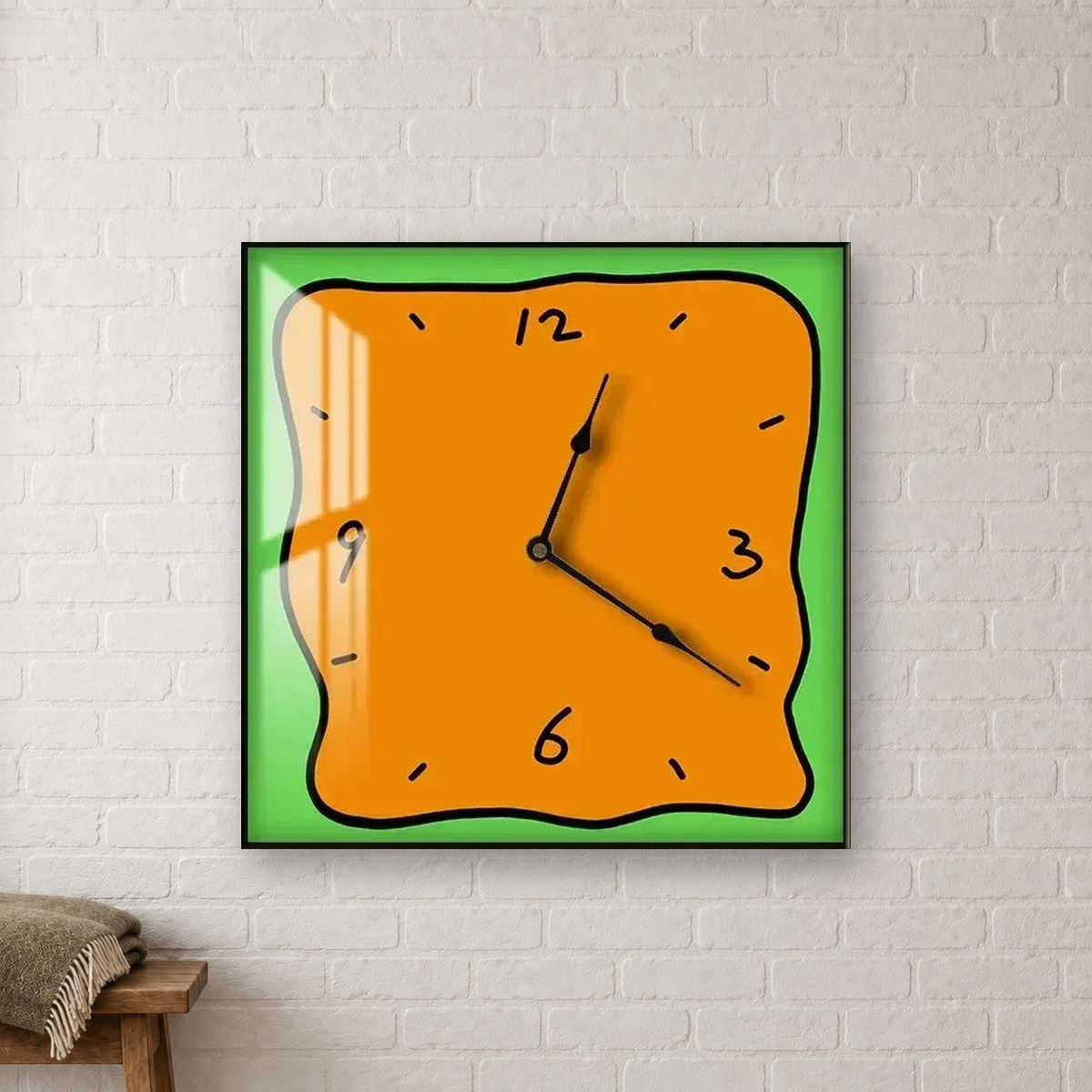Square wall clock with a wavy doodle-style outline, an orange face and a green border, hanging centred on a white brick wall