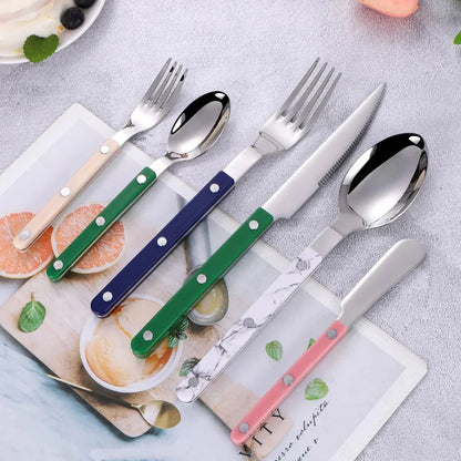 Mixed handled flatware pieces in beige, green, navy, white marble-look and pink laid on a printed card on a gray table, seen from above
