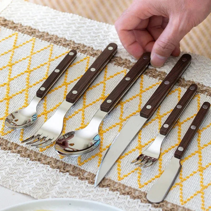 Brown wood-grain look handled six piece flatware set on a woven yellow table runner, a hand touching one piece