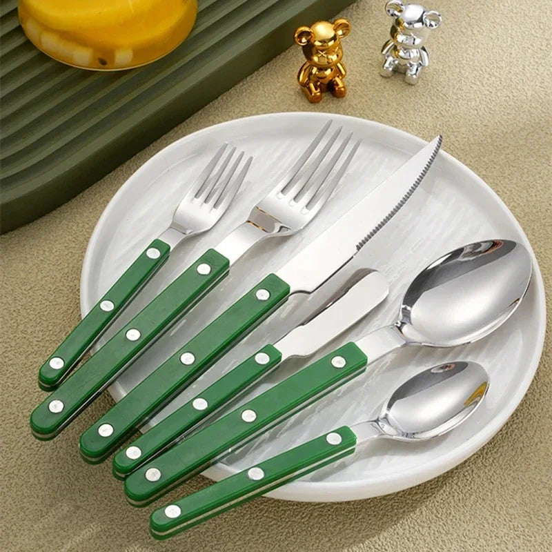 Green handled six piece flatware set fanned across a white plate, two small metallic bear figurines behind