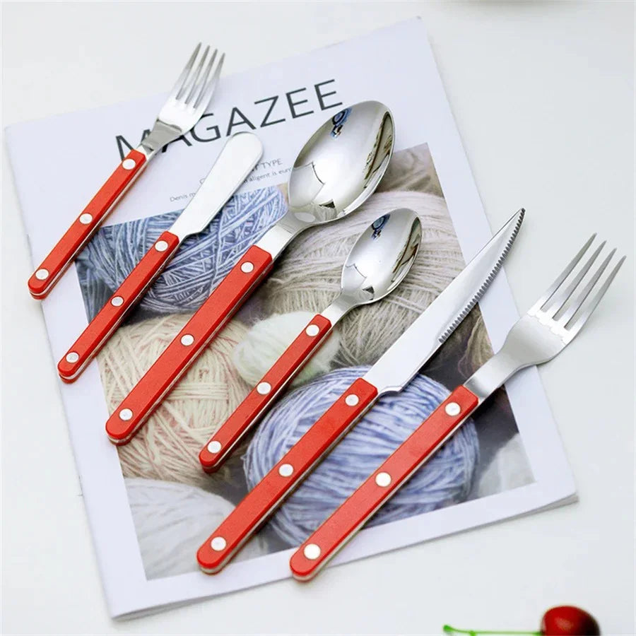 Red handled six piece flatware set laid on a magazine page over balls of yarn