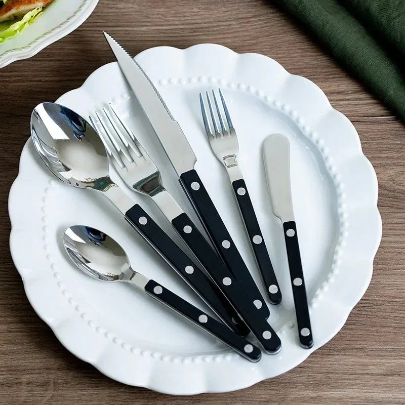 Black handled six piece flatware set on a scalloped white plate on a wooden table